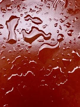 Water droplets scattered on a textured bright red glossy surface Stock Photos