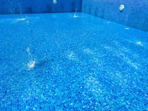 Water drops create splashes on the surface of the pool while bright sunlight  Stock Photos