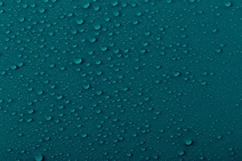 Water drops on a dark teal surface create a pattern showing reflections and.. Stock Photos