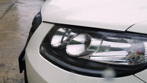 Water drops during rain roll down the glass of the front headlight of a car. Video stock 313370851