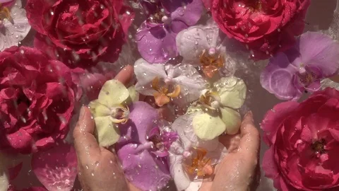 Water drops falling down on romantic roses and orchids flowers in woman hands. 動画素材 116965950