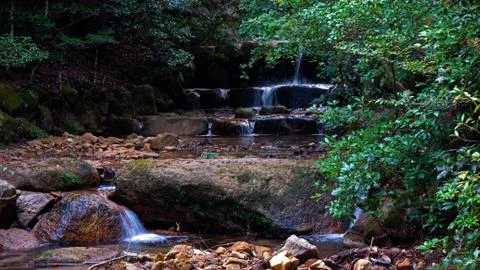 A water fall flows over rocks in a lush green autumn Japanese forest Stock Photos