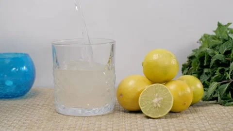 Water falling inside a glass half-filled with a refreshing lemon juice Stock Footage 153070639