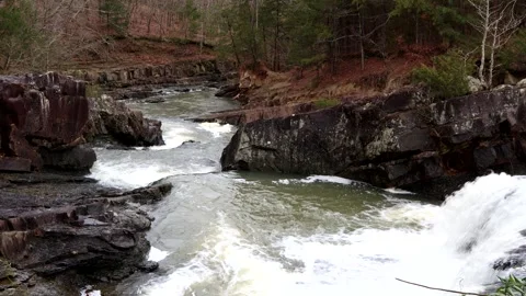 Water falls and gushes over a rocky riverbed in a mountain setting, 4k 動画素材 337434856