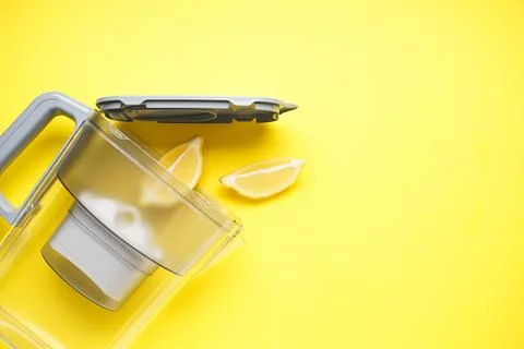 Water filter jug with lemon on a yellow background. Top view. Stock Photos