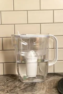 Water filter pitcher on a kitchen countertop with tiles in background Stock Photos