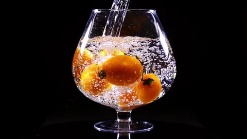 Water flowing into the big wineglass with orange tomatoes in extreme slow motion Stock Footage