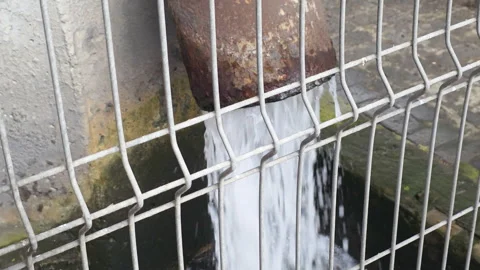 Water flowing forcefully from an old rusty metal pipe into a concrete drain Stock Footage 335273649