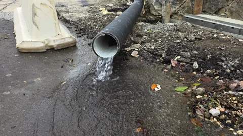 Water flowing from a large corrugated plastic drain pipe onto an asphalt road at Vídeo Stock 329754419