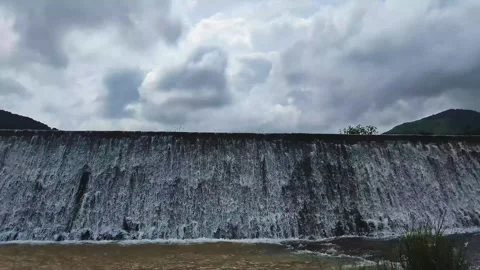 Water Flowing Over Small Dam Wall Under Cloudy Sky Stock Footage 327722063