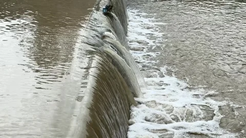 Water flowing over small dam outdoors creating foam and strong current Stock Footage 336959932