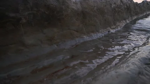 Water flowing quietly alongside a dark rocky coastal cliff wall. Stock Footage 337408072