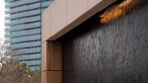 Water flows along black stone wall with orange backlight. Modern fountain in a Stock Footage 129658627