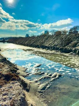 Water flows along the riverbank while clouds move across the sky. Buildings a Stock Photos