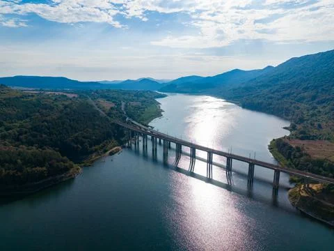 Water flows beneath a bridge on a river surrounded by hills under a cloudy sk Stock-Fotos