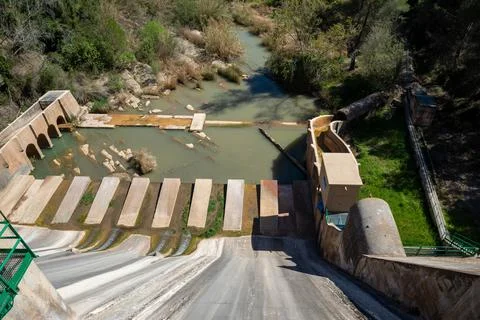 Water flows down a dam structure into a river below Stock Photos