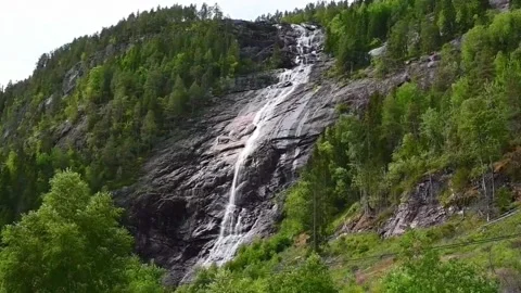 Water flows down rocky cliffs in Norway surrounded by green trees during da.. Stock Footage 340214798