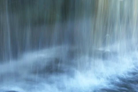 Water flows down a small wall with reflections behind. Blue-white blurred water Stock Photos