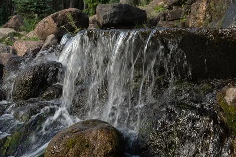 Water flows down a stone tier of an artificial waterfall in a public park Stock Photos