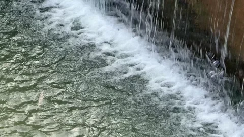 Water flows down the threshold of a concrete river channel, creating foam Stock Footage 325516931