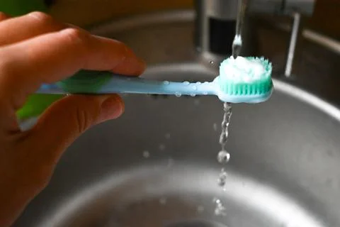 Water flows down the toothbrush and falls into the sink Stock Photos