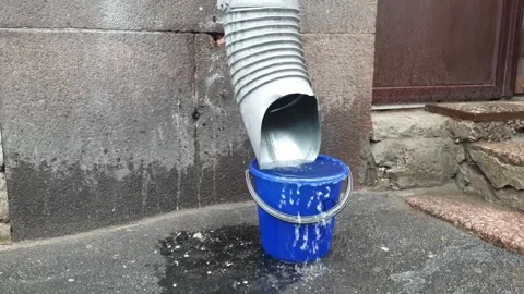 Water flows from a downpipe into a plastic bucket during rain Video stock 249382701