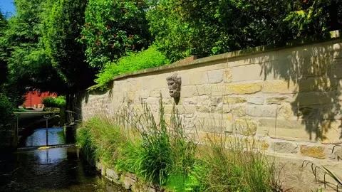 Water flows gently alongside a stone wall with greenery in a quiet area Stock-Footage 347460259