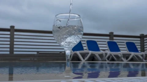Water flows into a glass next to the pool in slow motion. Healthy lifestyle. Stock Footage 155224741