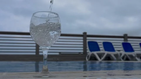 Water flows into a glass next to the pool in slow motion. Healthy lifestyle. Stock Footage 155224776