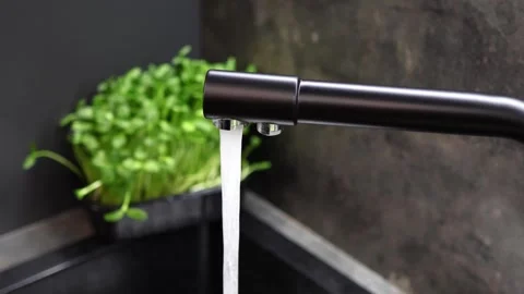 Water flows gracefully from a sleek black faucet in a stylish kitchen 스톡 동영상 296313164