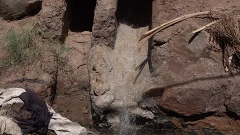 Water flows harmoniously from a hole beside the dry earth, with some rocks. Stock Footage 321946544