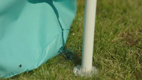 Water flows from hole from inflatable blue pool stand on green grass summer day Stock Footage 243771234