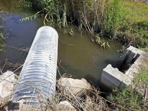 Water flows from a large drainage pipe into an irrigation canal at an ecolo.. Stock-Fotos