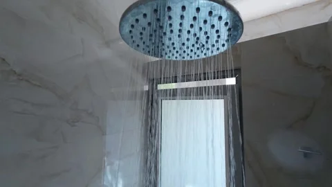 Water flows from a modern ceiling rain shower in a tiled bathroom, with natural Video stock 313795769
