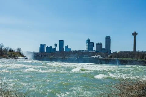 Water flows at Niagara Falls while city buildings stand in the background u.. Fotos de archivo