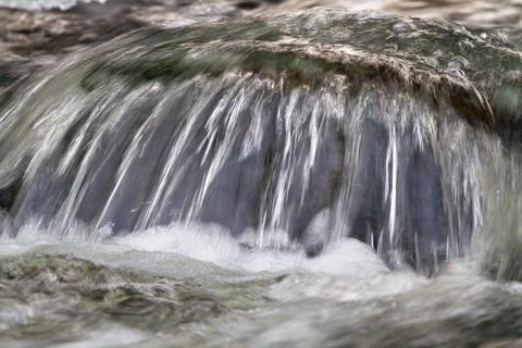 Water flows over a boulder in the river Stock Photos