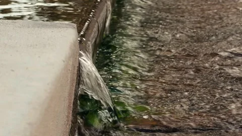 Water Flows Over a Concrete Ledge Into a Rocky Stream Vídeos de archivo 339127054