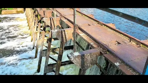 Water flows over a dam as sunlight reflects on the surface near a river in a nat Video stock 326115735