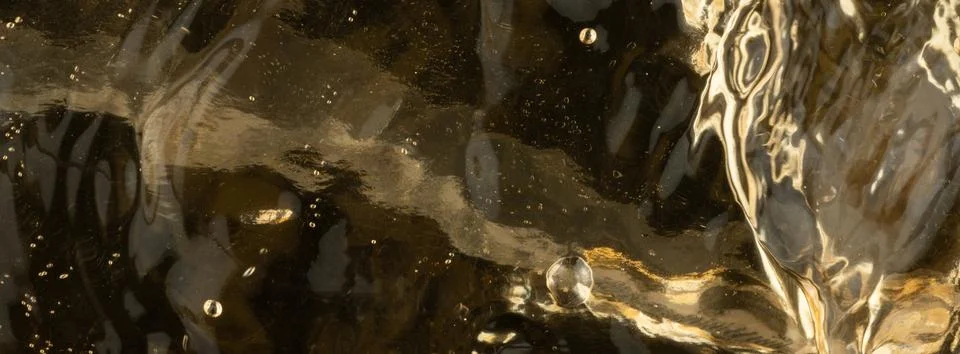 Water flows over dark surface and creates bubbles under bright light Stock Photos