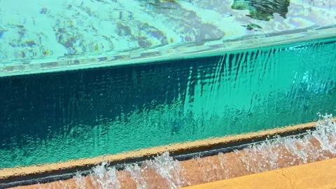 Water flows over the edge of a swimming pool during a bright sunny day with Stock Footage 332967971