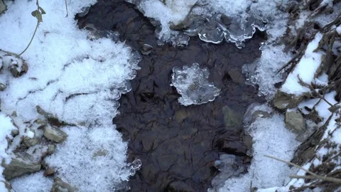 Water flows over ice in a winter setting with snow covering the ground Stock Footage 327590985