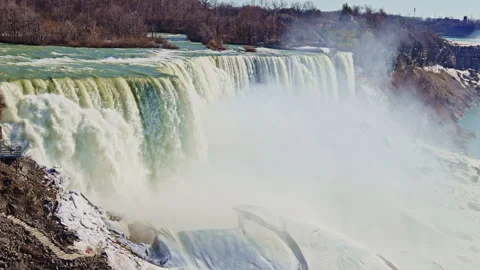 Water flows over Niagara Falls with mist rising into the air on a sunny day Stock Footage 334157766