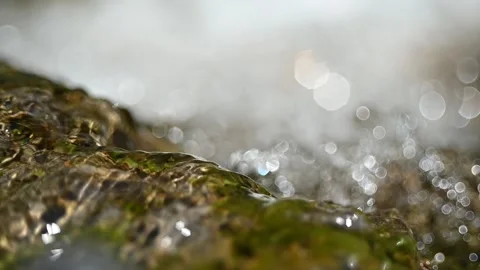 Water flows over a rock in front of the bokeh of a waterfall (slow motion) Stock-Footage 219636109