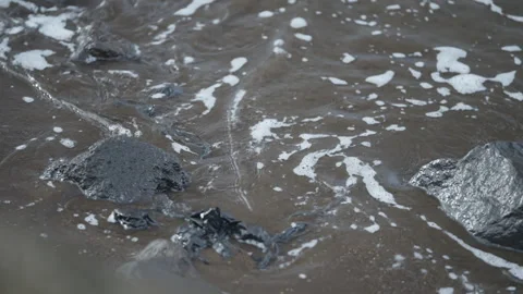 Water flows over rocks creating foam on the shoreline. Video stock 328026714