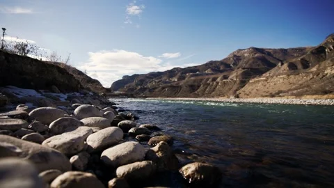 Water flows over rocks by mountains, creating a picturesque natural landscape Stock Footage 272212161
