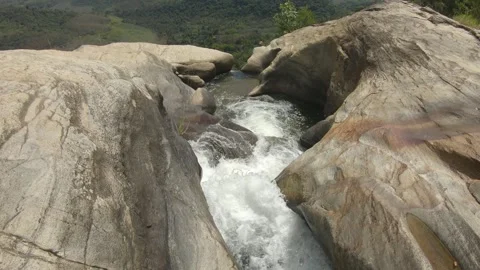 Water flows over rocks revealing a valley under clear skies in Sri Lanka 스톡 동영상 307862432