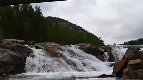 Water flows over rocks in a river in Norway near a mountain under cloudy sk.. Stock Footage 340214593