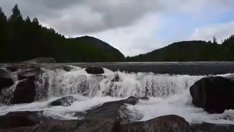 Water flows over rocks in a river surrounded by trees and mountains in Norw.. Stock Footage 340214797