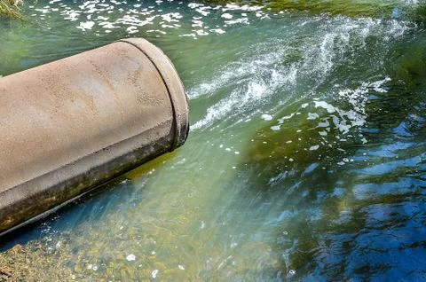 Water flows from the pipe into the river. Stock Photos