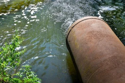 Water flows from the pipe into the river. Stock Photos